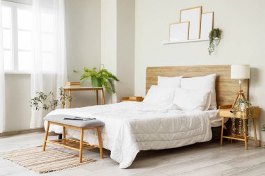 Konforlu yatağı, çiçekleri ve ahşap komodiniyle aydınlık yatak odasının içi.