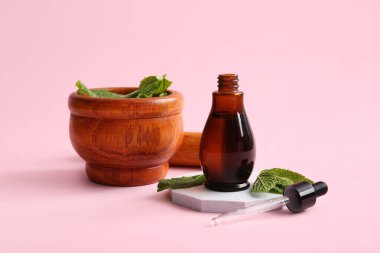 Pembe arka planda bir şişe yağ, harç, alçı standı ve nane yaprakları, yakın plan.