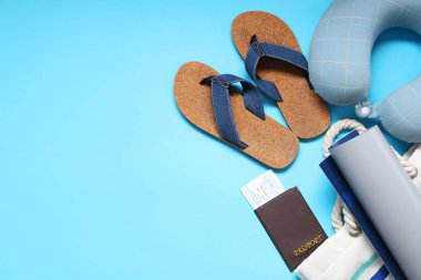Seyahat yastığı, bilet, cüzdan, harita, çanta ve parmak arası terlikler mavi arka planda
