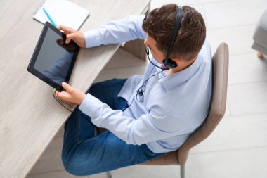 Evde çalışan tablet bilgisayarı ve kulaklığı olan genç bir çocuk.