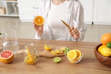 Mutfakta eritilmiş su hazırlamak için farklı narenciye meyveleri kesen genç bir kadın.