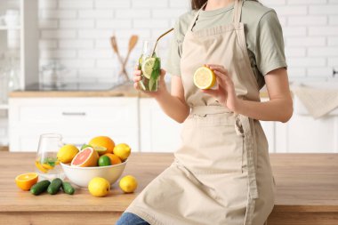 Genç bir kadın mutfakta salatalık ve nane ile doldurulmuş limon şişesi tutuyor.