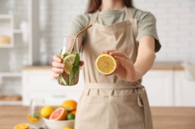 Genç bir kadın mutfakta salatalık ve nane ile doldurulmuş limon şişesi tutuyor.