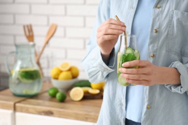 Genç bir kadın mutfakta salatalık ve nane ile doldurulmuş su şişesi tutuyor.