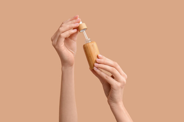 Руки женщины с бутылкой косметического средства на коричневом фоне