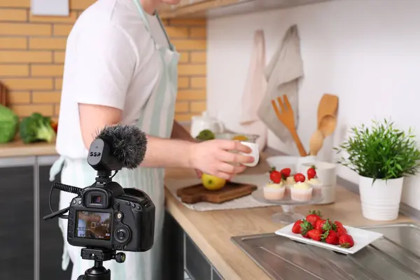 stock image Young man with sweet muffins and fresh strawberries recording cooking video in kitchen