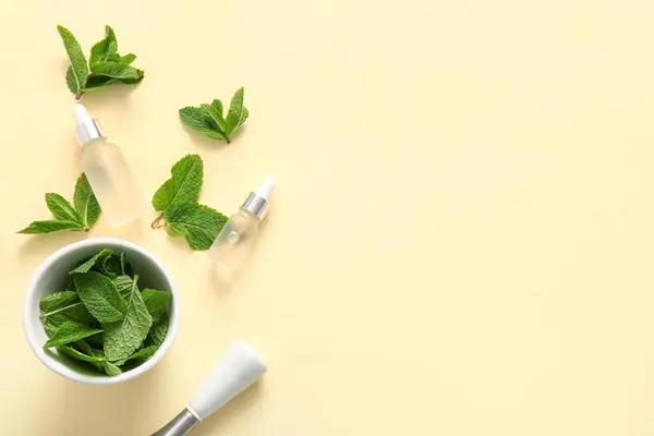 stock image Bottles of essential oil, mortar, pestle and mint leaves on beige background