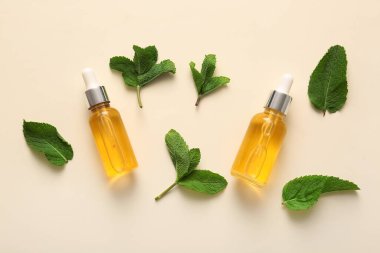 Temel nane yağı şişeleri ve bej arka planda yeşil yapraklar
