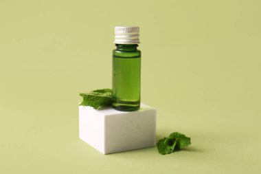 Bir şişe nane yağı, alçı standı ve yeşil arka planda yeşil yapraklar, yakın plan.