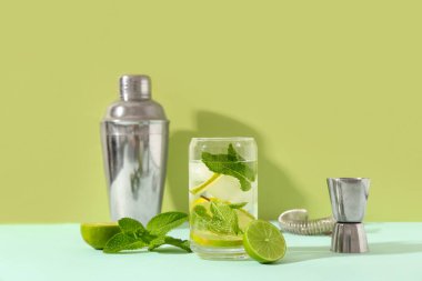 Bir bardak taze mojito. Kokteyl karıştırıcı ve yeşil arka planda mavi masada jigger.