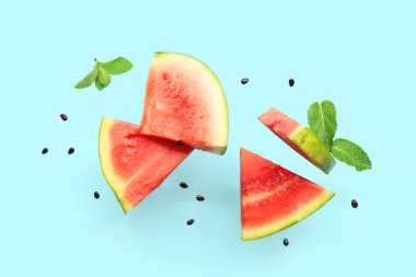 Uçan taze karpuz parçaları ve mavi arka planda nane ve tohumlar.