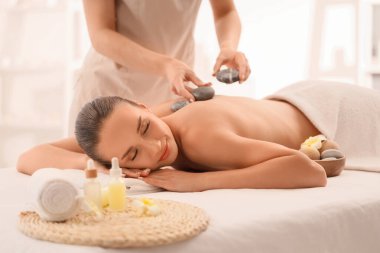 Genç bir kadın kaplıcada sıcak taşlarla masaj yaptırıyor.