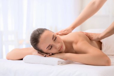 Rahatlamış genç bir kadın spa salonunda terapist tarafından masaj yaptırıyor.
