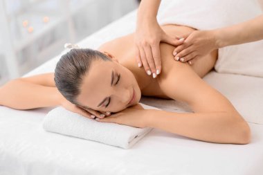 Rahatlamış genç bir kadın spa salonunda terapist tarafından masaj yaptırıyor.