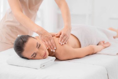 Spa salonunda terapistin masaj yaptırdığı genç bir kadın.