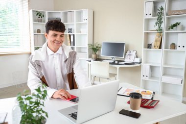 İş yerinde hesap makinesi ve laptop ile çalışan erkek muhasebeci.