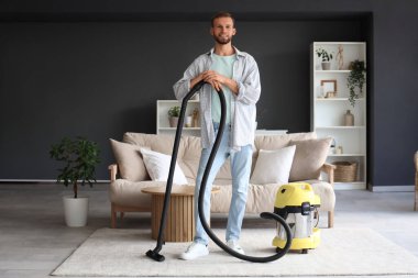 Odasında elektrik süpürgesi olan erkek hademe.