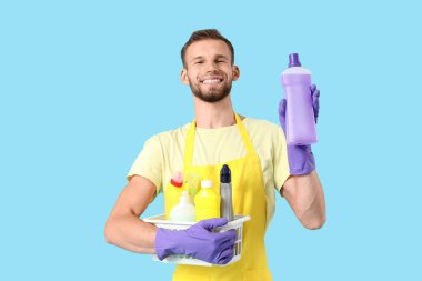 Mavi arka planda temizlik malzemeleri olan sepet tutan erkek hademe.
