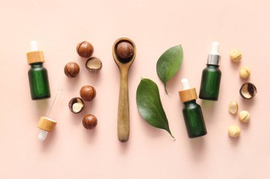 Macadamia fındığı, ahşap kaşık, yeşil yapraklar ve pembe arka planda kozmetik ürünler.