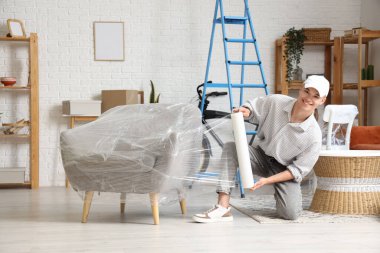 Genç adam evinde streç filmle koltuğu sarıyor.