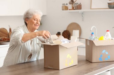 Mutfakta kutular dolusu çöpü olan yaşlı bir kadın. Atık sıralama kavramı