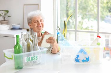 Mutfaktaki deftere çöp tenekeleri yazan son sınıf kadını. Atık sıralama kavramı