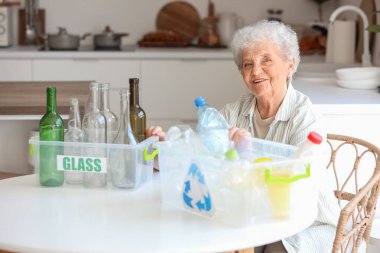 Mutfakta elinde çöp bidonları olan yaşlı bir kadın. Atık sıralama kavramı