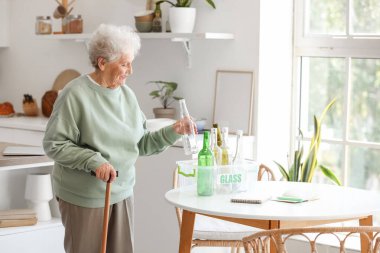 Mutfaktaki masada cam çöp kutusuna sopa yerleştiren son sınıf öğrencisi bir kadın.