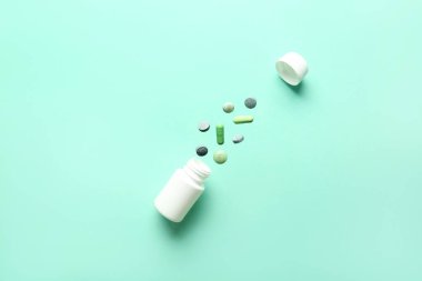 Turkuaz arka planda uçan yeşil haplarla dolu bir şişe. Üst görünüm