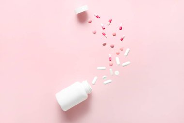 Pembe arka planda uçan haplarla dolu bir şişe. Üst görünüm