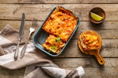 Lezzetli enchilada ve ahşap arka planda çatal bıçaklı kompozisyon