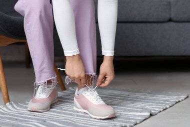 Şık ayakkabılı ve pembe pantolonlu bir kadın evde ayakkabı bağı bağlıyor.