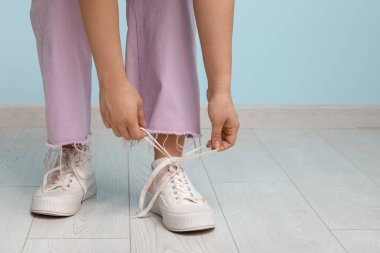 Şık ayakkabılı ve pembe pantolonlu bir kadın mavi arka plana ayakkabı bağlıyor.