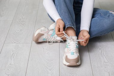Renkli spor ayakkabılı ve kot pantolonlu bir kadın evde ayakkabı bağcıklarını bağlıyor.