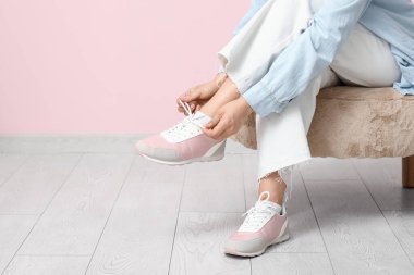 Pembe arka plana ayakkabı bağlayan şık ayakkabılı ve kot pantolonlu bir kadın.