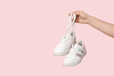 Pembe arka planda şık spor ayakkabıları olan kadın eli.