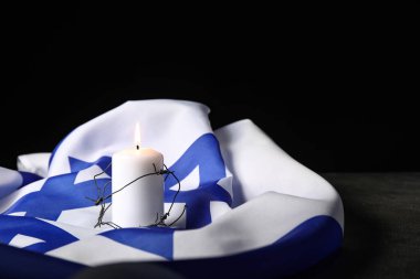 Dikenli telle yanan mum ve koyu arkaplanda İsrail bayrağı. Soykırım Anma Günü