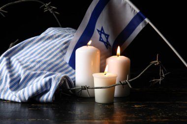 Mahkum üniforması, yanan mumlar, dikenli teller ve arka planda İsrail bayrağı. Soykırım Anma Günü