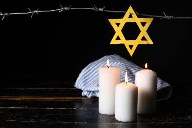 Mahkûm üniforması, Davut Yıldızı, karanlık arka planda yanan mumlar ve dikenli teller. Soykırım Anma Günü