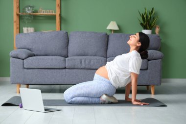 Güzel hamile kadın oturma odasında yoga yapıyor.