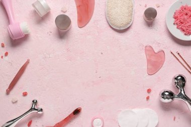 Farklı yüz masajı araçlarından yapılmış çerçeve ve pembe zemin üzerinde kozmetik ürünler kavanozları