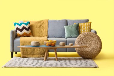 Rahat gri kanepe, sehpa ve sarı arka planda hasır puf.