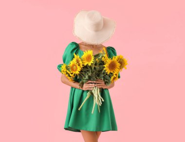 Hasır şapkalı güzel bir kadın pembe arka planda bir buket ayçiçeğiyle