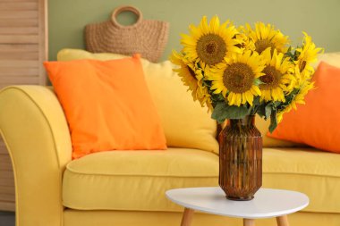 Sarı kanepenin yanındaki sehpanın üzerinde güzel ayçiçeği buketi vazosu, yakın plan.