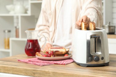 Adam ekmek kızartma makinesine ekmek dilimleri koyuyor mutfaktaki ahşap masaya.