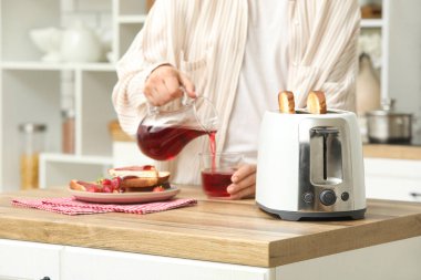 Beyaz ekmek kızartma makinesi ve mutfakta tahta masaya meyve suyu döken bir adam.