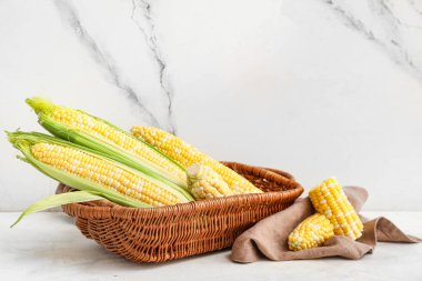 Taze mısır koçanları ve beyaz masanın üzerinde peçeteyle dolu bir sepet.