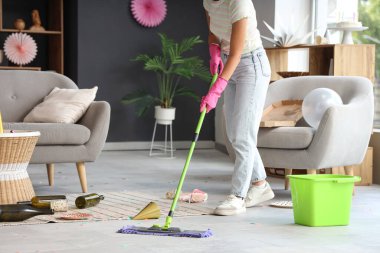 Doğum günü partisinden sonra dağınık odada yerleri paspaslayan genç kadın.