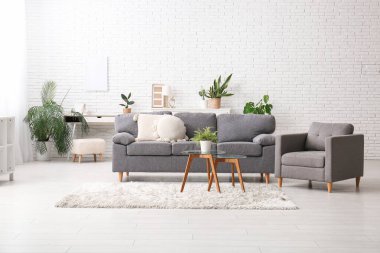 Oturma odasının içindeki beyaz tuğla duvarın yanındaki kanepe, masa ve bitkiler.