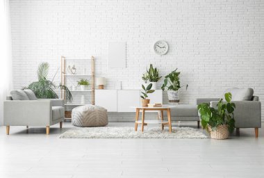 Oturma odasının içindeki beyaz tuğla duvarın yanında farklı bitkiler var.